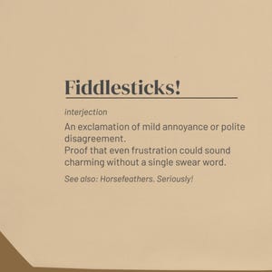 May include: A beige card featuring the word Fiddlesticks! in dark brown text, followed by the definition: interjection, An exclamation of mild annoyance or polite disagreement. Proof that even frustration could sound charming without a single swear word. See also: Horsefeathers. Seriously!