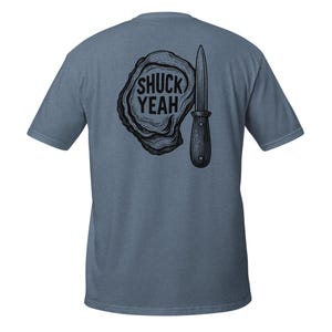 May include: A blue t-shirt with a black graphic of an oyster shell and a shucking knife. The text "SHUCK YEAH" is inside the oyster shell. The shirt is made of a soft material.