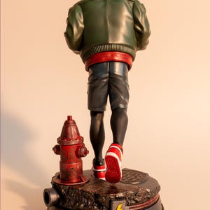 May include: A figurine of a character in a green jacket, red hood, and shorts, walking away. The figure is standing on a base with a red fire hydrant and a manhole cover. The figure's sneakers are red and white.