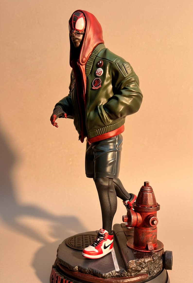May include: A figurine of a character in a red and black mask, wearing a green bomber jacket, black shorts, and red and white sneakers. The figure is posed near a red fire hydrant.