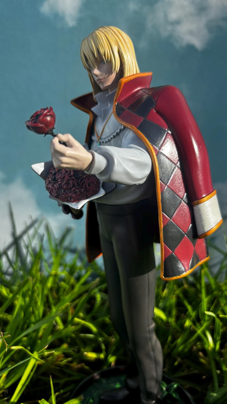 K&ouml;nnte beinhalten: Figur eines Charakters mit blonden Haaren, der ein wei&szlig;es Hemd, eine dunkle Hose und einen roten Mantel mit schwarz-roten Rautenmustern tr&auml;gt. Die Figur h&auml;lt eine rote Rose und einen Rosenstrau&szlig;. Der Hintergrund ist ein blauer Himmel und gr&uuml;nes Gras.