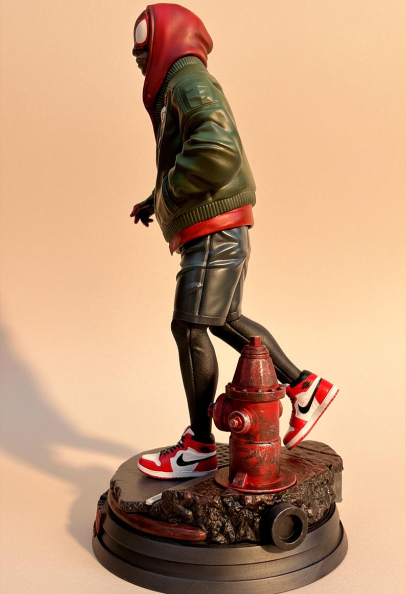 May include: A figurine of a superhero in a red and green outfit, black shorts, and red and white sneakers. The figure is standing on a base with a red fire hydrant. The superhero is wearing a red hood and a green jacket.