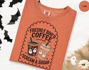 May include: A yam-colored t-shirt with a Halloween-themed graphic. The design features two coffee cups with ghost illustrations and the text "Freshly Boo'd Coffee served with Scream & Sugar". The shirt is a Comfort Colors brand.