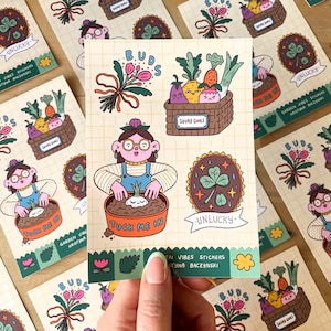 May include: A collection of illustrated stickers with a garden theme. The stickers feature a person planting a bulb, vegetables in a basket labeled "Squad Goals", and a four-leaf clover with the word "Unlucky".
