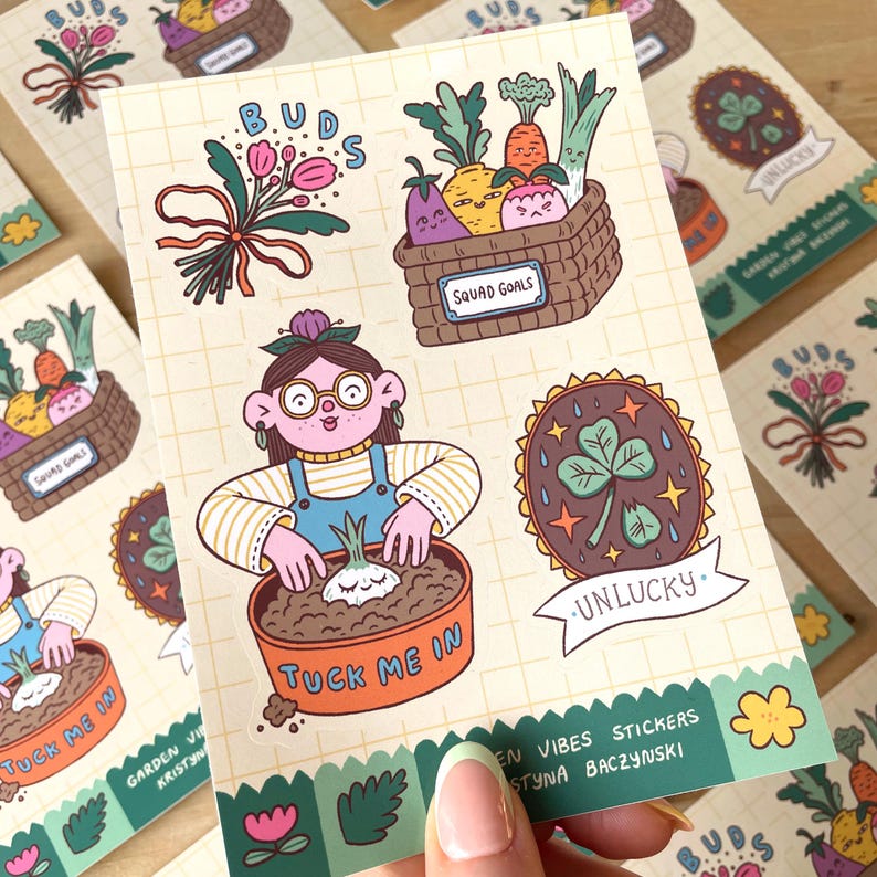 May include: A sheet of colorful stickers with a garden theme. Designs include a basket of vegetables, a gardener, a four-leaf clover, and the text "Tuck Me In" and "Squad Goals". The stickers are on a grid-patterned background.