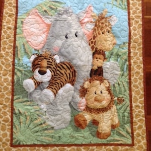 May include: A colorful baby quilt with a jungle theme. The quilt features a gray elephant, a brown tiger, a yellow giraffe, a brown monkey, and a brown lion. The quilt is surrounded by a brown and tan border with a giraffe print.