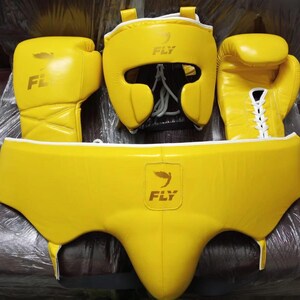 Può includere: Un set completo di attrezzatura da boxe gialla, tra cui guantoni, caschetto e conchiglia protettiva. I guantoni e il caschetto presentano la scritta "FLY". Il set è realizzato in materiale resistente ed è progettato per la protezione.