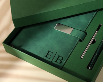Puede incluir: Un juego de regalo verde en una caja verde. El juego incluye un cuaderno de cuero verde con un cierre de metal plateado, un bolígrafo y un bolígrafo de metal plateado. El cuaderno está grabado con las iniciales "E/B".
