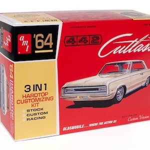 May include: A model kit box for a '64 Oldsmobile Cutlass. The box is red, yellow, and white, with an illustration of the car. Text includes "3 in 1 Hardtop Customizing Kit" and "Authentic Model".