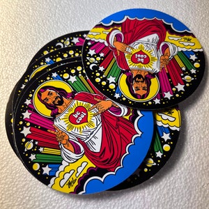 Może przedstawiać: Stos okrągłych naklejek z kresk&oacute;wkową ilustracją postaci z aureolą, ubranej w czerwone szaty i pokazującej znak pokoju. Postać ma serce z napisem "be cool" na piersi. Naklejki mają czarną obw&oacute;dkę z gwiazdami i kolorowymi akcentami.