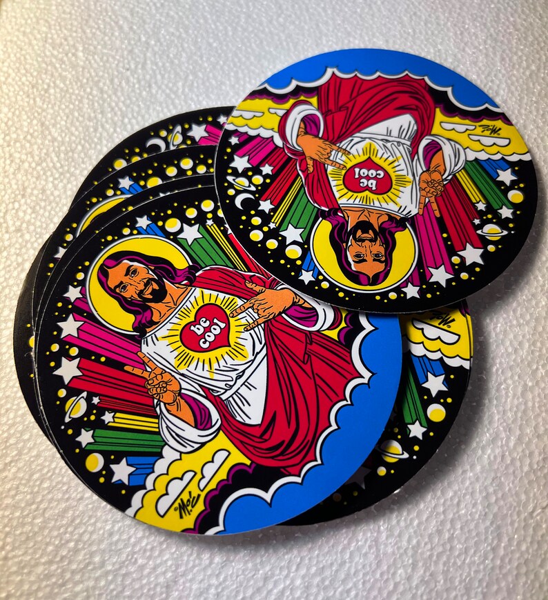 Może przedstawiać: Stos okrągłych naklejek z kresk&oacute;wkową ilustracją postaci z aureolą, ubranej w czerwone szaty i pokazującej znak pokoju. Postać ma serce z napisem "be cool" na piersi. Naklejki mają czarną obw&oacute;dkę z gwiazdami i kolorowymi akcentami.