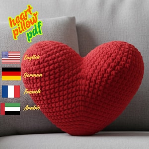 May include: A handmade, red heart-shaped pillow. The pillow is made of a textured, crocheted material. Text in the image reads "heart pillow pdf". The pillow is resting on a gray surface.