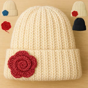 May include: Cream-coloured knitted beanie with a large red crocheted flower on the front. Additional beanies in cream and navy blue are shown, each with a crocheted flower in red or blue. The beanies have a ribbed knit design.