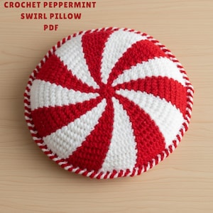 May include: A round, crocheted pillow with a peppermint swirl design. Alternating red and white stripes radiate from the center. The pillow has a white and red stitched border. The text "CROCHET PEPPERMINT SWIRL PILLOW PDF" is at the top.