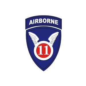 May include: A shield-shaped patch featuring a dark blue background with a white border. At the top, a tab reads AIRBORNE in white letters. The center displays a red circle containing the white number 11, flanked by two white stylized wings.