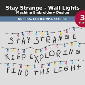 Peut inclure: Motif de broderie machine avec les phrases "Stay Strange", "Keep Exploring" et "Find the Light". Le motif comprend des guirlandes d'ampoules colorées. Le texte "Stay Strange - Wall Lights" est en haut.