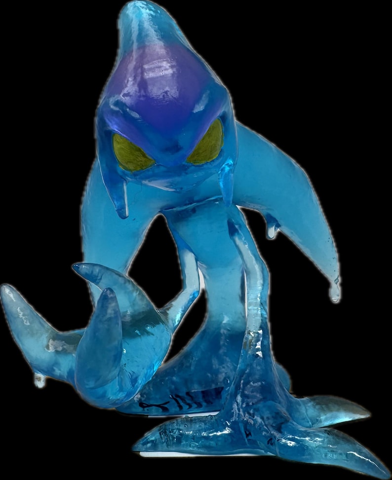 May include: A translucent blue figurine of a creature with a teardrop-shaped head, yellow eyes, and flowing appendages. The figure has a darker blue area on its head and is posed on a black background.