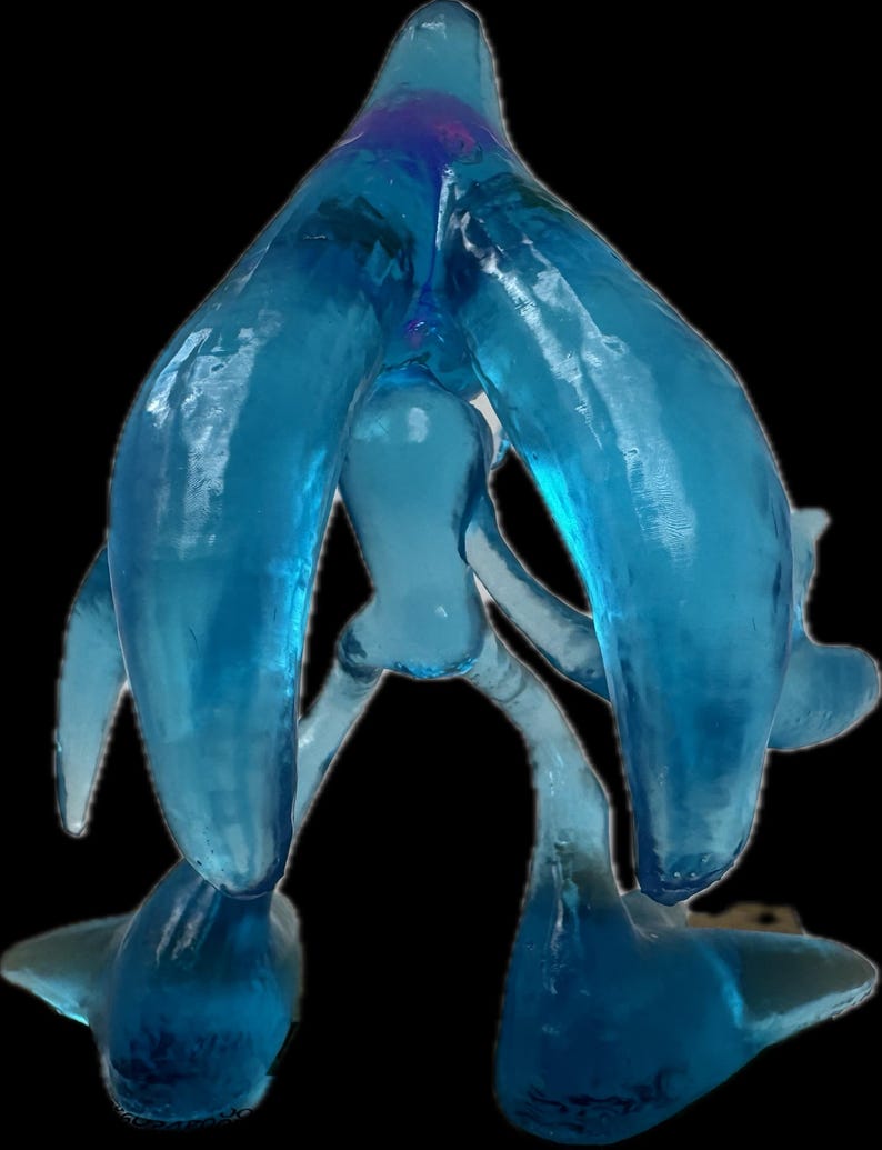May include: A translucent, light blue art glass sculpture with an abstract design. The sculpture has a central, rounded form with two large, curved arms extending upwards and outwards. The base features two rounded feet, and the overall shape is organic.