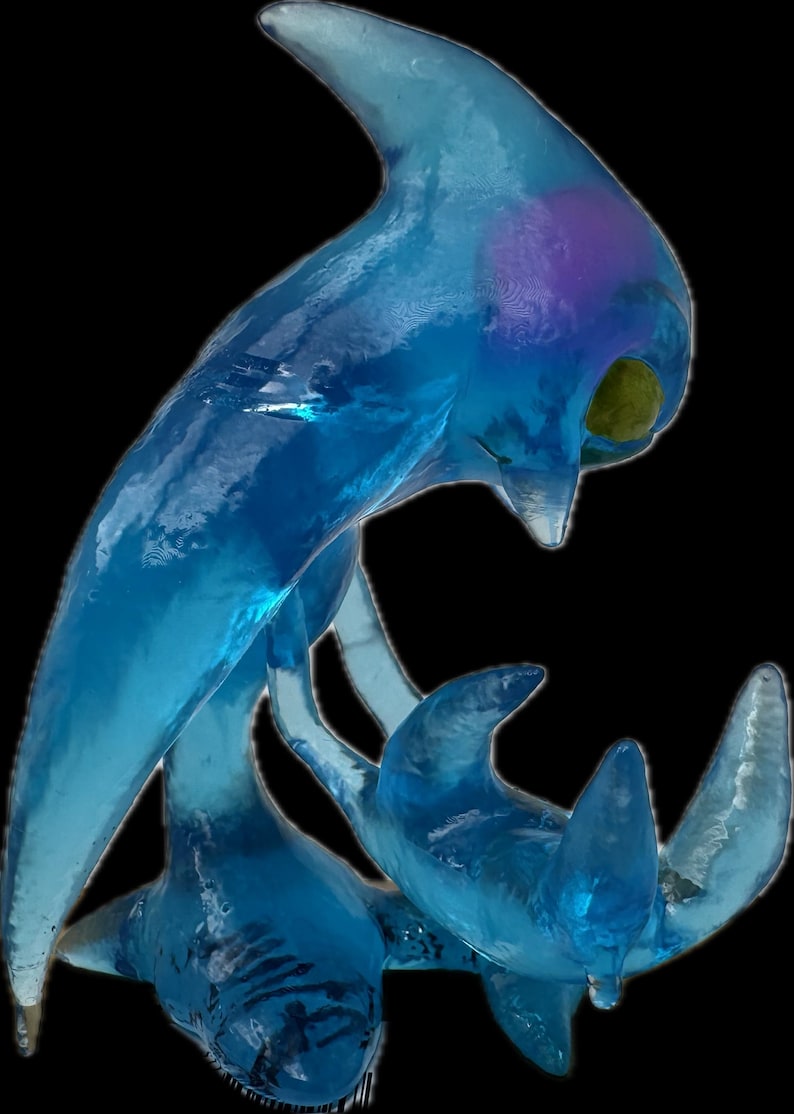 May include: A translucent blue sculpture of a stylized aquatic creature, possibly a dolphin or whale, with a sleek, flowing form. The sculpture has a smooth, glossy finish and is set against a black background.