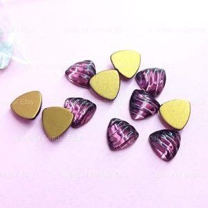 Peut inclure: Des perles triangulaires dorées et violettes sont disposées sur une surface rose clair. Certaines perles sont dorées unies, d'autres violettes avec un motif tourbillonnant. Idéal pour la création de bijoux ou l'artisanat.