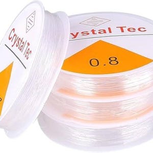 May include: Spools of clear, elastic beading cord. The spools have white labels with the text "Crystal Tec" and an orange triangle with the number "0.8". The cord is tightly wound on the spools, ready for jewelry making or other crafts.
