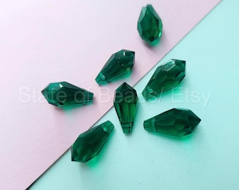 Peut inclure: Perles en forme de goutte d'eau facettées vert émeraude. Ces perles ont un sommet pointu et un fond plat. Les perles sont disposées sur un fond rose et turquoise. Les perles mesurent environ 2 cm de long.