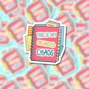 A colorful vinyl sticker featuring an illustration of stacked spiral notebooks and planners with tabs. The main text reads 'THIS IS MY ORGANIZED CHAOS' in white, yellow, and teal lettering on a pink notebook cover. The sticker shows various planning elements like to-do lists, checkboxes, and organizational tabs in bright colors including pink, yellow, green, and blue.