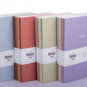 May include: Four sets of softcover notebooks in blue, terracotta, sage green, and purple. Each set is wrapped in a white paper band featuring the text Hoos, a smiley face logo, and product details including 8 pack, A5, 80g ruled inner paper, 80 pages.