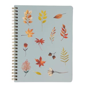 Pode incluir: Um caderno espiralado com capa azul clara adornada com ilustrações coloridas de folhas de outono. As folhas são em tons de laranja, amarelo e castanho. A encadernação em espiral do caderno é prateada.