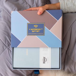 May include: A notebook gift set in a geometric patterned box with the text "Notebook Gift Set". The box is open, revealing a light blue notebook with a white band and the brand name "Hoos". The set includes two notebooks with 80 pages each.