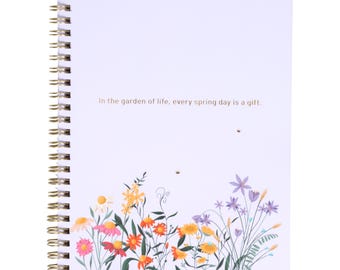 May include: A spiral-bound notebook with a white cover featuring a floral design in shades of pink, orange, yellow, and purple. The text "In the garden of life, every spring day is a gift" is printed on the cover.