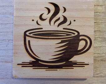 May include: A square wooden coaster with a laser-etched design of a coffee cup. The cup is filled with coffee and steam is rising from the top. The coaster is made of light-colored wood.