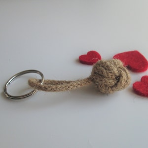 May include: A brown rope keyring with a knotted ball at the end. The keyring is surrounded by three red felt hearts.