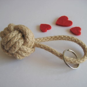 May include: A brown rope keychain with a knotted ball and a silver key ring. The keychain is decorated with four red felt hearts.