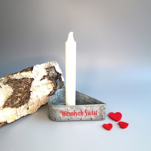 May include: A galvanized metal candle holder with a white candle, the text "Wesołych Świąt" in red, and three small red felt hearts. A piece of birch bark is on the left. The background is a solid gray.