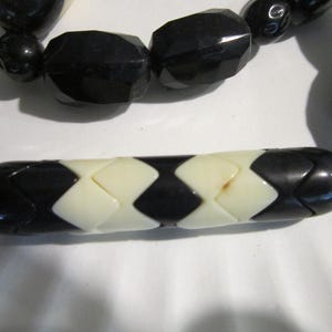 May include: A black and white beaded necklace with a geometric pattern. The necklace is made of round and rectangular beads.