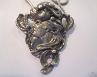 May include: Silver pendant necklace featuring a detailed, stylised design of a woman's face with flowing hair and floral accents.