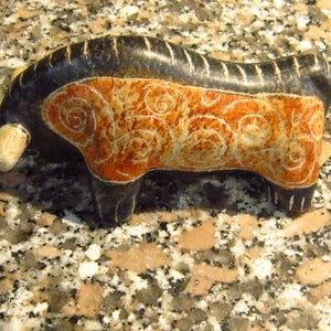 Könnte beinhalten: Eine schwarze und orangefarbene Steinskulptur eines Bullen mit komplizierten Wirbelmustern. Der Bulle steht auf einer Granitoberfläche.