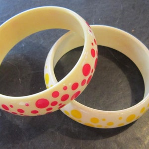 May include: Two white plastic bangles with red and yellow polka dots. The bangles are stacked on top of each other.