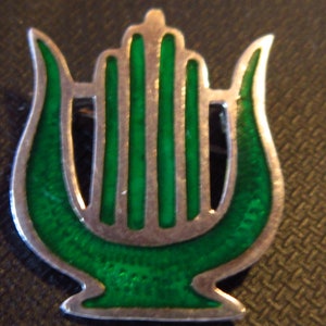 May include: A silver lyre brooch with green enamel. The lyre is a musical instrument with a body shaped like a harp.