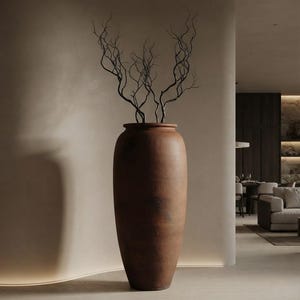 Op de afbeelding: Een hoge, cilindrische vloervaas van terracotta met een matte, aardebruine afwerking en een licht uitlopende rand. De vaas bevat verschillende dunne, donkere, gedraaide takken die omhoog steken en een opvallend, vertakt silhouet vormen.