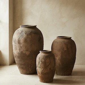 May include: Three large, dark brown terracotta vessels with wide, circular openings and tapered bases. Each vessel features a textured, ribbed surface pattern created by vertical and diagonal indentations across the exterior clay body.