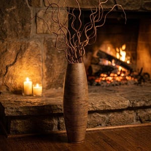 May include: A tall, cylindrical brown vase with a textured, wrapped surface finish. The vase is filled with several long, slender, and naturally twisted brown branches that extend upwards in a sprawling, organic arrangement.