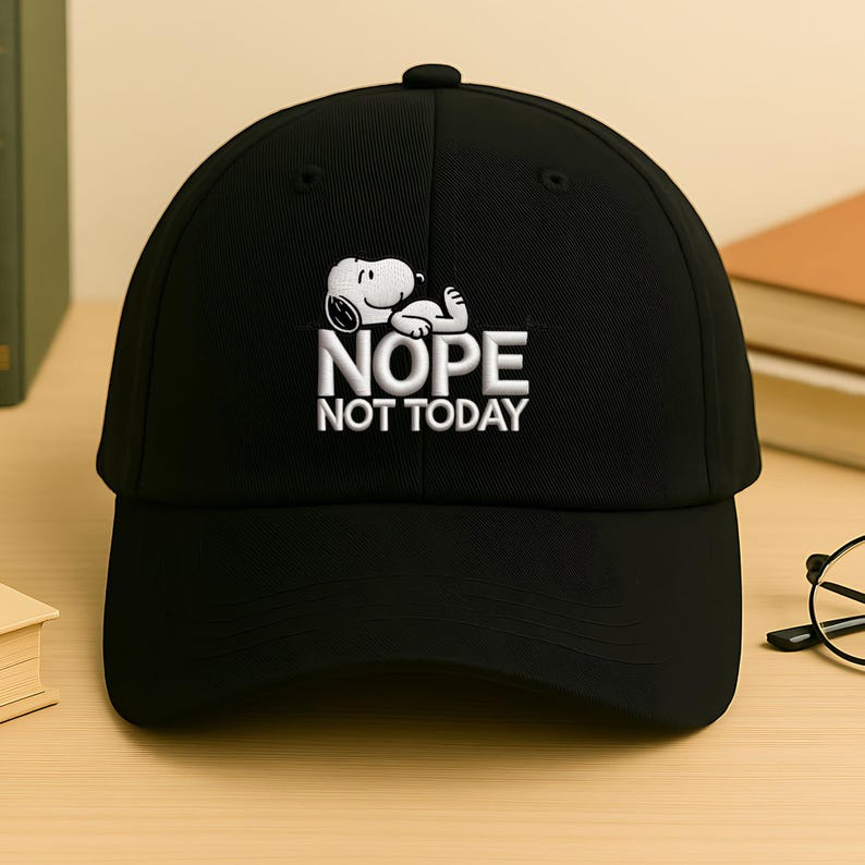 May include: Black baseball cap featuring a white embroidered Snoopy graphic with the text "NOPE NOT TODAY." The cap has a curved brim and a button on top. A fun and casual accessory.