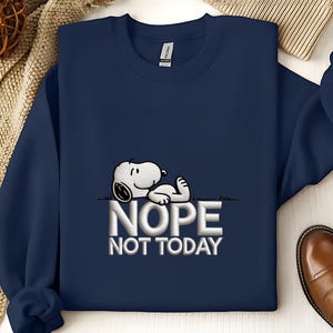 May include: Navy blue sweatshirt featuring a graphic of Snoopy lying down with the words "NOPE NOT TODAY" in white. The sweatshirt is a crew neck style and appears to be made of a soft material.