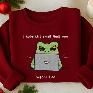 May include: A maroon sweatshirt features a green frog with an angry expression using a laptop. The text reads "I hope this email finds you before I do." The design includes "clack" sound effects.