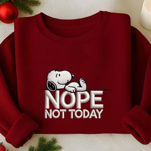 May include: A maroon sweatshirt featuring a white Snoopy graphic lying down, with the text "NOPE NOT TODAY" in white block letters. The sweatshirt has a crew neck and long sleeves. The design is centered on the chest.