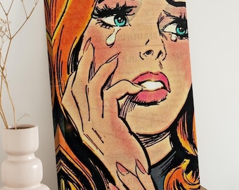 May include: Pop art canvas print featuring a close-up of a crying woman. The artwork showcases a woman with orange hair, blue eyes, and pink lips, with a tear rolling down her cheek. The style is reminiscent of vintage comic book illustrations.