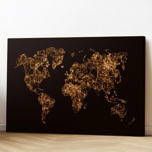 May include: A black canvas print featuring a world map design. The map is rendered with interconnected golden lines, creating a network effect across the continents. The artwork is displayed against a white wall and rests on a wooden floor.