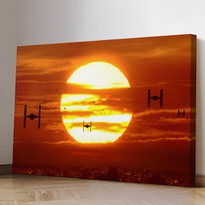 May include: A canvas print depicting a sunset scene with a large, bright sun and several black TIE fighter silhouettes. The sky is filled with orange and red hues, creating a dramatic and cinematic effect. The artwork is mounted on a wooden frame.